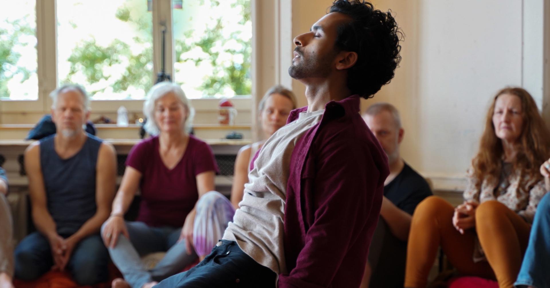 A man in circle with eyes closed, held in deep presence by others around him